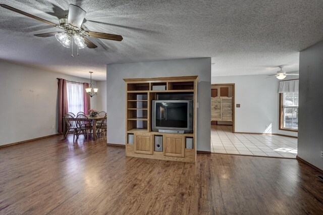 unfurnished living room with ceiling fan with notable chandelier, a textured ceiling, and light wood-type flooring