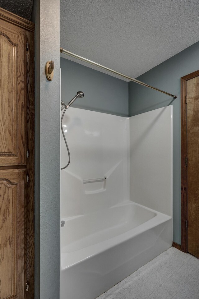 bathroom with a textured ceiling and tub / shower combination