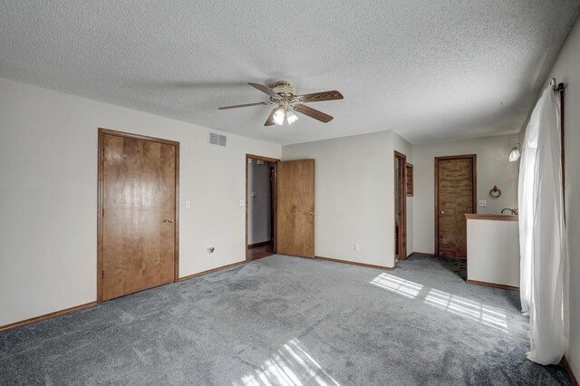 unfurnished bedroom with ceiling fan, light carpet, a textured ceiling, and multiple closets