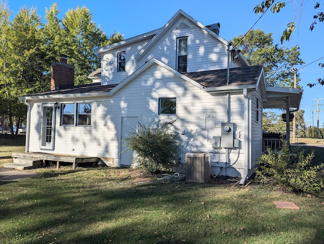 rear view of property featuring central air condition unit and a lawn