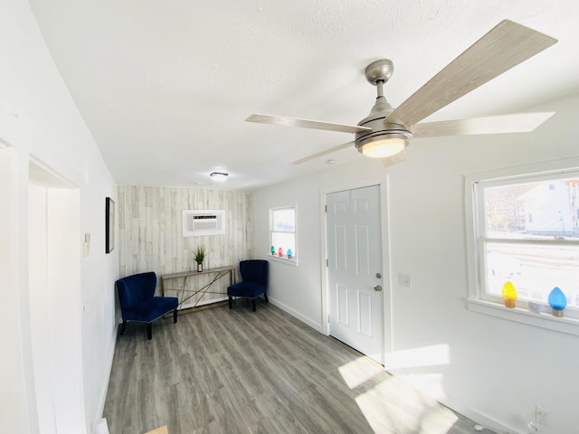 foyer with ceiling fan, wooden walls, a wall unit AC, light hardwood / wood-style floors, and a textured ceiling