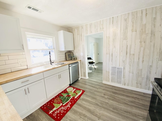 kitchen featuring white cabinetry, stainless steel dishwasher, wooden counters, and sink