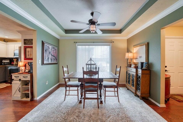 dining area featuring ceiling fan, a raised ceiling, ornamental molding, and dark hardwood / wood-style flooring