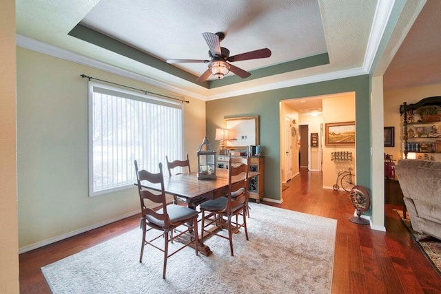 dining room with hardwood / wood-style flooring, ornamental molding, a raised ceiling, a textured ceiling, and ceiling fan