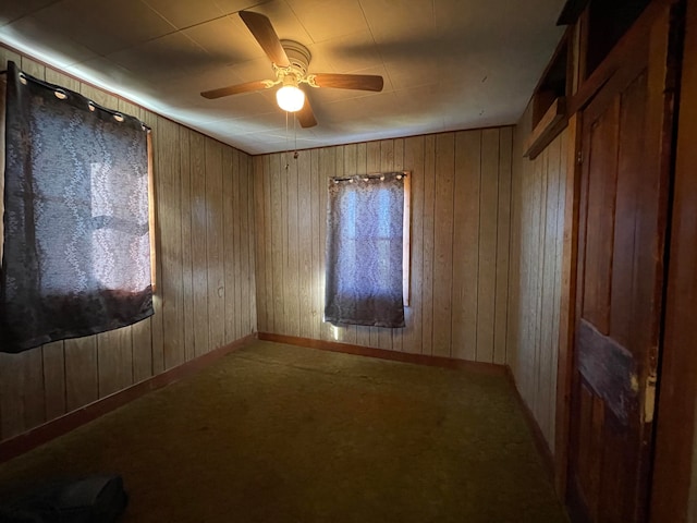 carpeted empty room with ceiling fan and wood walls