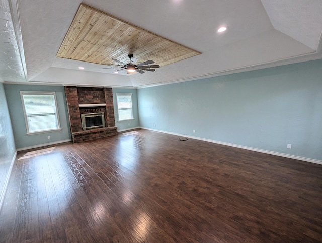 unfurnished living room with a raised ceiling, a brick fireplace, ceiling fan, dark wood-type flooring, and crown molding