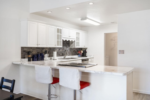 kitchen with decorative backsplash, kitchen peninsula, sink, a breakfast bar, and white cabinets