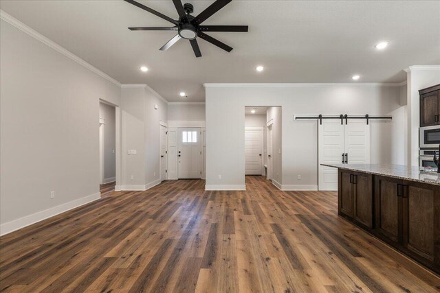 unfurnished living room featuring crown molding, dark hardwood / wood-style floors, a barn door, and ceiling fan