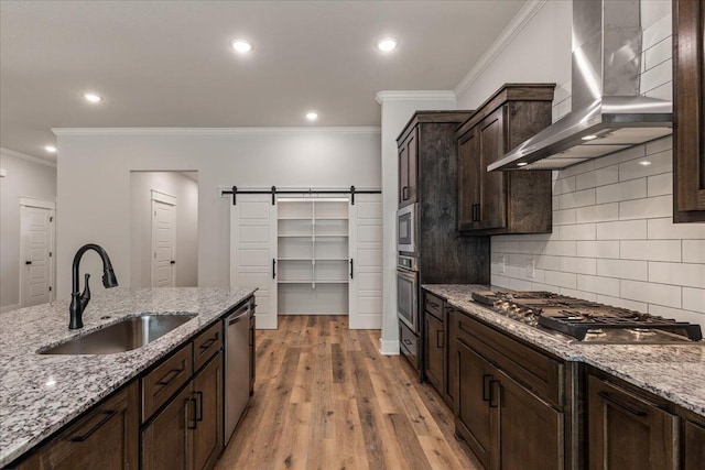 kitchen featuring appliances with stainless steel finishes, a barn door, light hardwood / wood-style floors, wall chimney exhaust hood, and sink