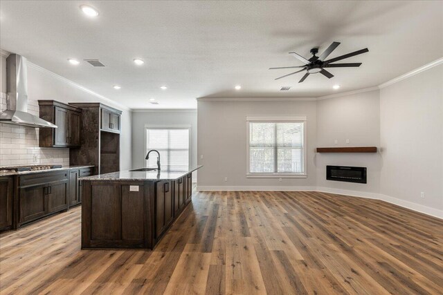 kitchen featuring a kitchen island with sink, wood-type flooring, ornamental molding, wall chimney exhaust hood, and sink