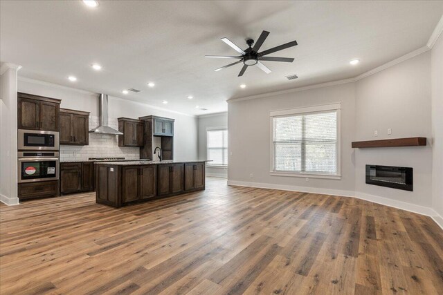 kitchen with hardwood / wood-style flooring, wall chimney exhaust hood, an island with sink, crown molding, and appliances with stainless steel finishes