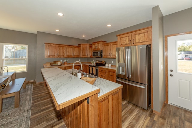 kitchen with a kitchen island with sink, dark wood-type flooring, sink, a kitchen bar, and appliances with stainless steel finishes