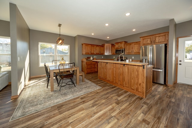 kitchen featuring a center island with sink, appliances with stainless steel finishes, dark hardwood / wood-style floors, and hanging light fixtures