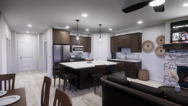 kitchen with a kitchen island, light wood-type flooring, pendant lighting, a stone fireplace, and stainless steel appliances