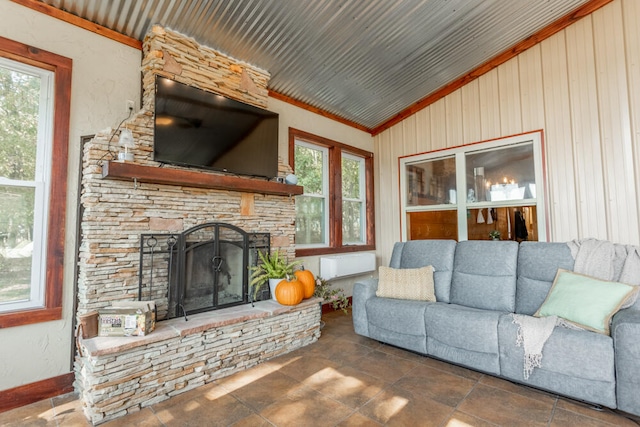 living room with a healthy amount of sunlight, a stone fireplace, ornamental molding, and vaulted ceiling