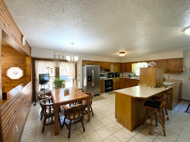 kitchen featuring a textured ceiling, wood walls, pendant lighting, stainless steel refrigerator with ice dispenser, and black range with electric cooktop