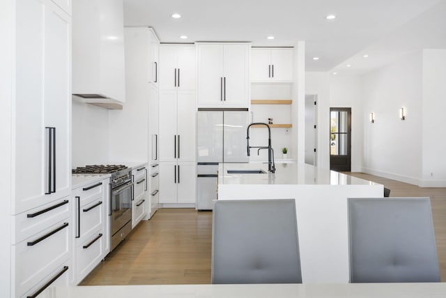 kitchen with custom exhaust hood, high end stainless steel range oven, white cabinetry, light hardwood / wood-style flooring, and sink