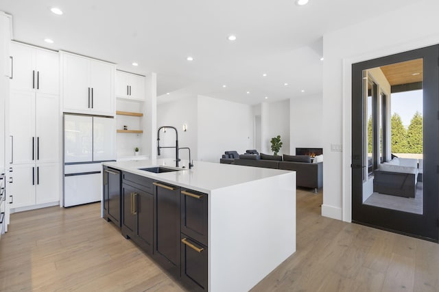 kitchen featuring sink, an island with sink, white fridge, and light wood-type flooring