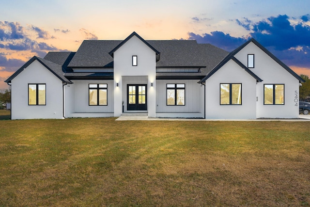 back house at dusk featuring french doors and a lawn