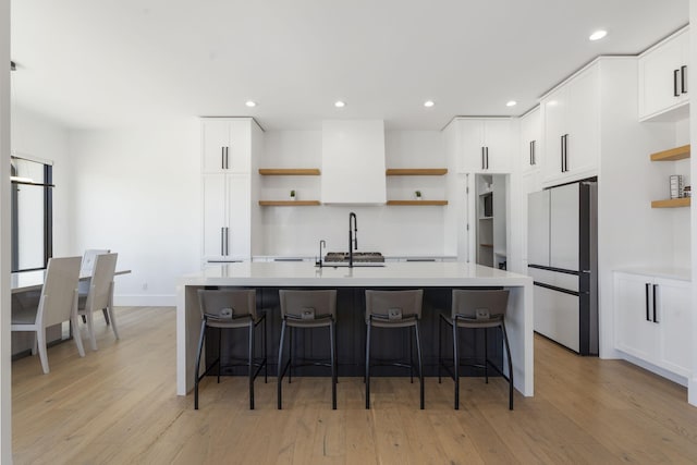 kitchen with a center island with sink, white cabinetry, light wood-type flooring, and stainless steel refrigerator