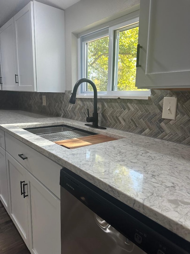 kitchen with light stone countertops, sink, white cabinetry, stainless steel dishwasher, and decorative backsplash