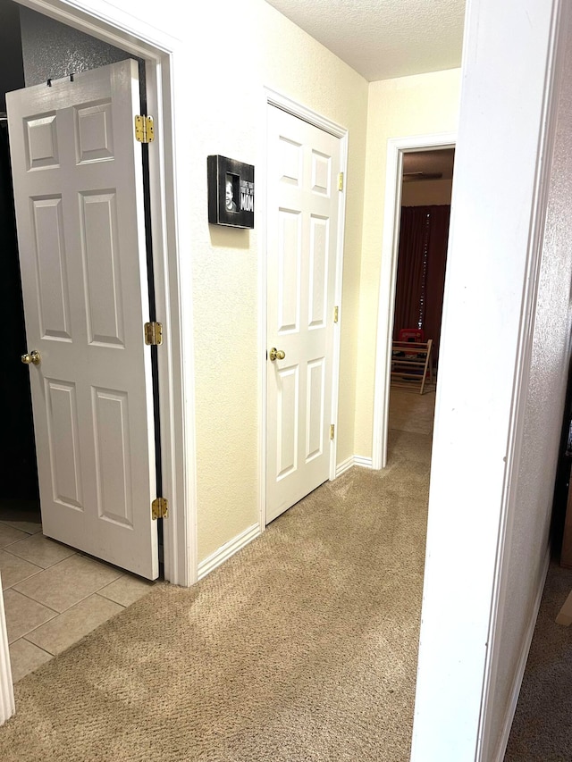 corridor with a textured ceiling and light colored carpet