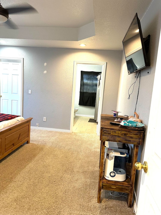 bedroom with ensuite bathroom, light colored carpet, and ceiling fan