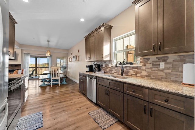 kitchen featuring light stone counters, light hardwood / wood-style flooring, stainless steel appliances, pendant lighting, and sink