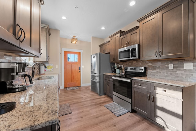 kitchen featuring light stone countertops, light wood-type flooring, sink, dark brown cabinetry, and stainless steel appliances