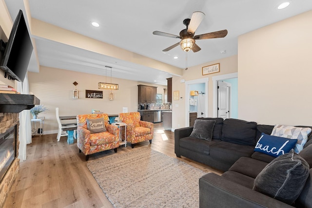 living area featuring recessed lighting, a ceiling fan, a stone fireplace, and light wood-style flooring