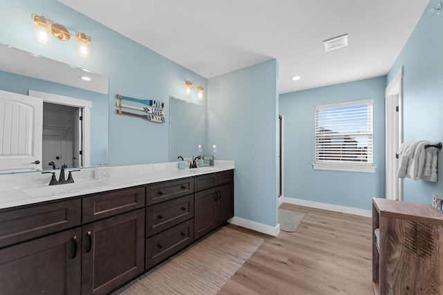 full bathroom with a sink, double vanity, visible vents, baseboards, and wood finished floors
