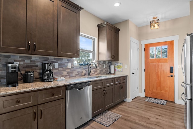 kitchen featuring a sink, stainless steel appliances, light wood-style floors, tasteful backsplash, and dark brown cabinetry