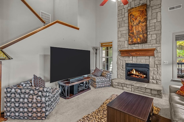 carpeted living room featuring a fireplace, a towering ceiling, and ceiling fan