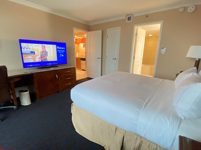 bedroom with crown molding, ensuite bathroom, and dark carpet