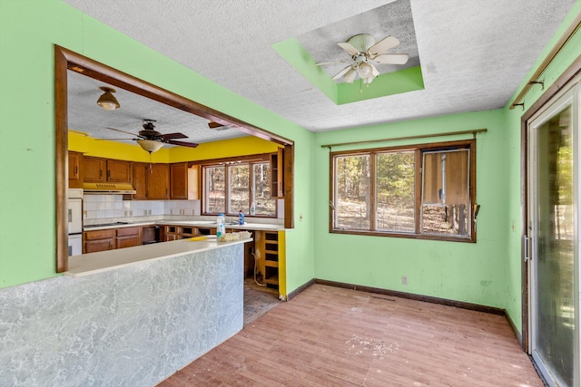 kitchen featuring brown cabinetry, a ceiling fan, a textured ceiling, and under cabinet range hood