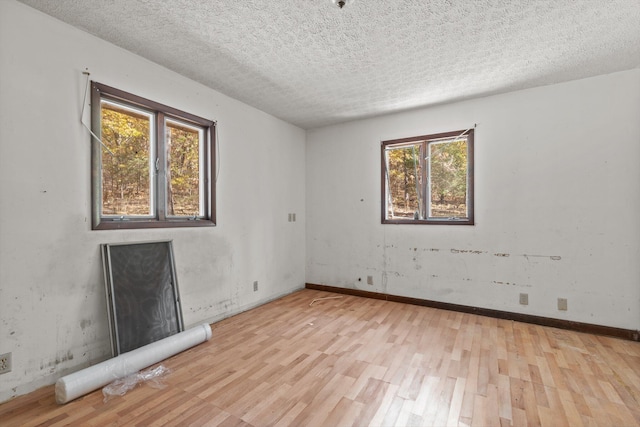 spare room with baseboards, light wood-type flooring, and a textured ceiling