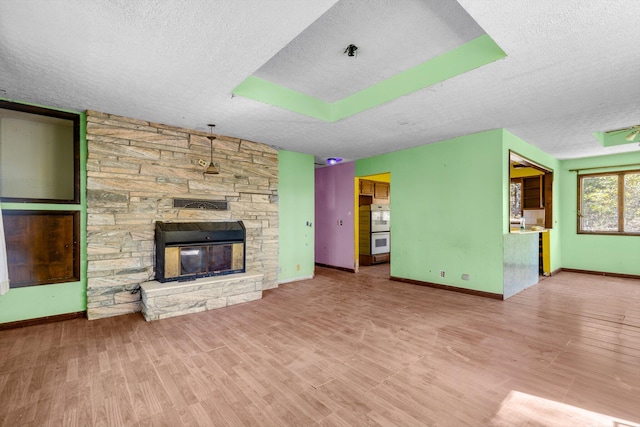 unfurnished living room featuring baseboards, a stone fireplace, a textured ceiling, and wood finished floors