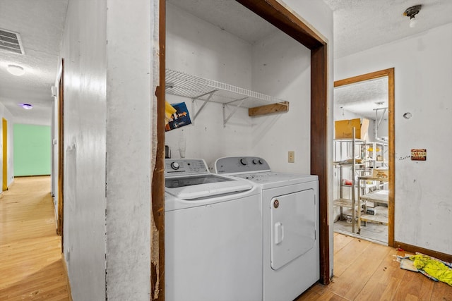 laundry room with laundry area, visible vents, washing machine and dryer, light wood-style floors, and a textured ceiling