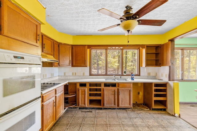 kitchen with a sink, light countertops, white double oven, tasteful backsplash, and under cabinet range hood