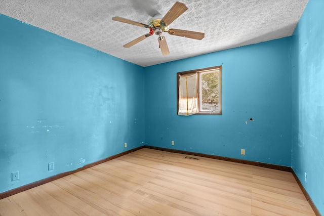 spare room featuring ceiling fan, a textured ceiling, baseboards, wood finished floors, and visible vents