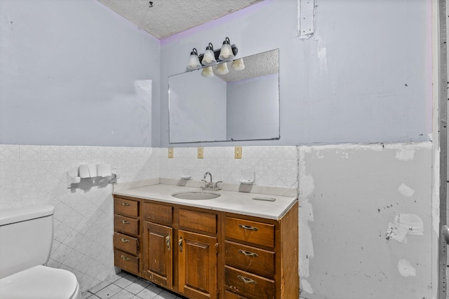 bathroom featuring a textured ceiling, tile walls, toilet, vanity, and tile patterned flooring