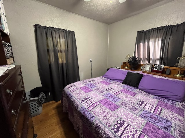 bedroom with a textured ceiling, wood-type flooring, and ceiling fan