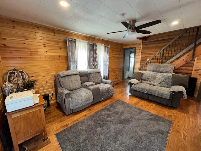 living room with hardwood / wood-style floors, wooden walls, and ceiling fan