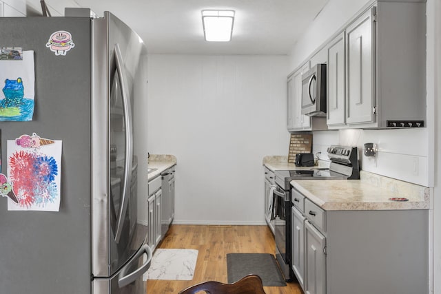 kitchen featuring gray cabinets, stainless steel appliances, light wood-type flooring, and backsplash