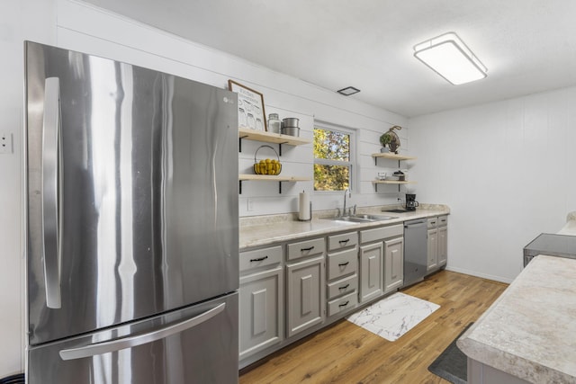 kitchen with light hardwood / wood-style flooring, wood walls, sink, gray cabinets, and stainless steel appliances