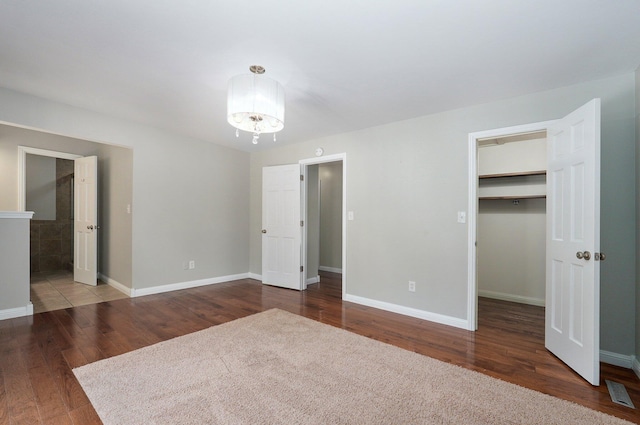 unfurnished bedroom featuring a walk in closet, a closet, an inviting chandelier, and hardwood / wood-style flooring