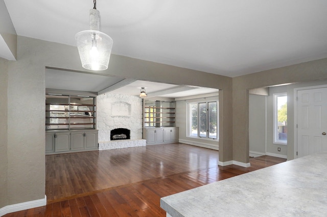 unfurnished living room featuring a stone fireplace and dark wood-type flooring