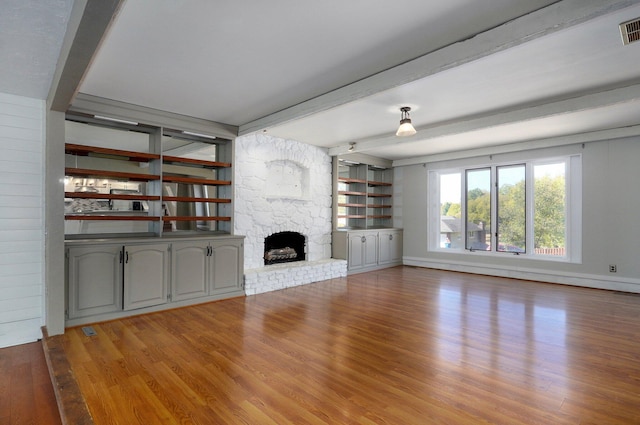 unfurnished living room featuring beam ceiling, a stone fireplace, and light hardwood / wood-style flooring