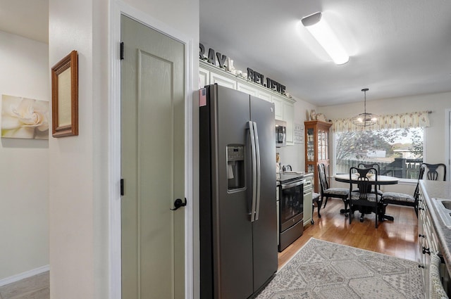 kitchen with white cabinetry, stainless steel appliances, light hardwood / wood-style flooring, a notable chandelier, and decorative light fixtures