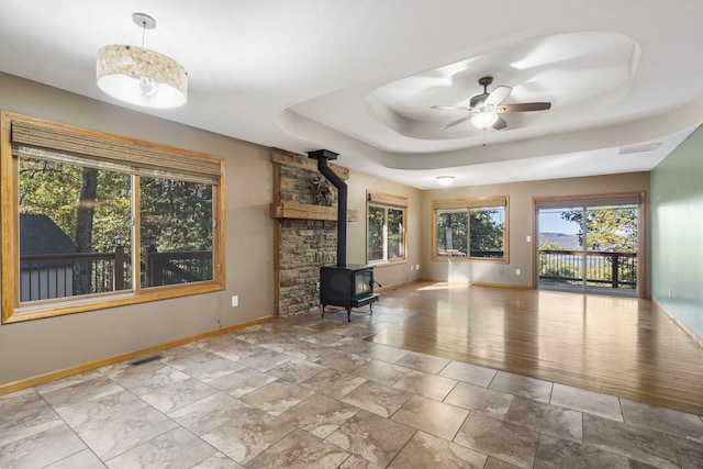 unfurnished living room featuring a tray ceiling, ceiling fan, and a wood stove